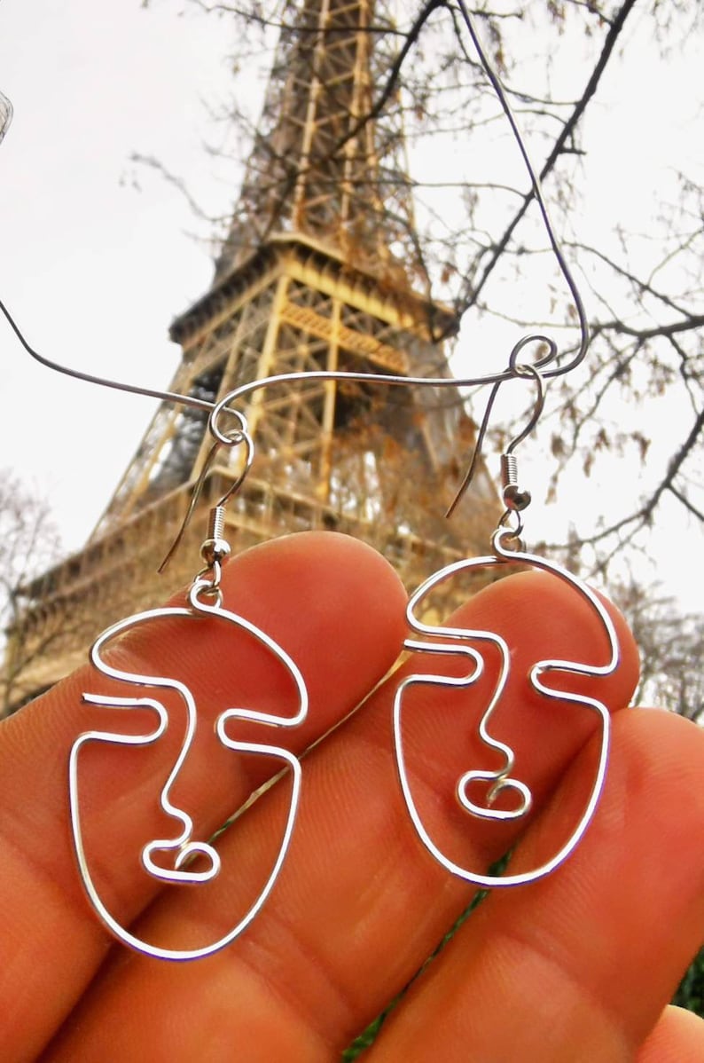 Zoom sur une femme avec des boucles d’oreilles abstraites en fil doré, une mise en situation idéale pour visualiser la taille et le style du bijou.