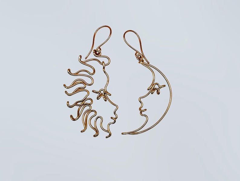Boucles d’oreilles asymétriques représentant le soleil et la lune, réalisées à la main en fil doré. Un bijou unique au design céleste, parfait pour un look mystique et élégant.