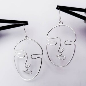Boucles d’oreilles suspendues devant la tour Eiffel, capturant l’inspiration artistique et la finesse du travail artisanal.