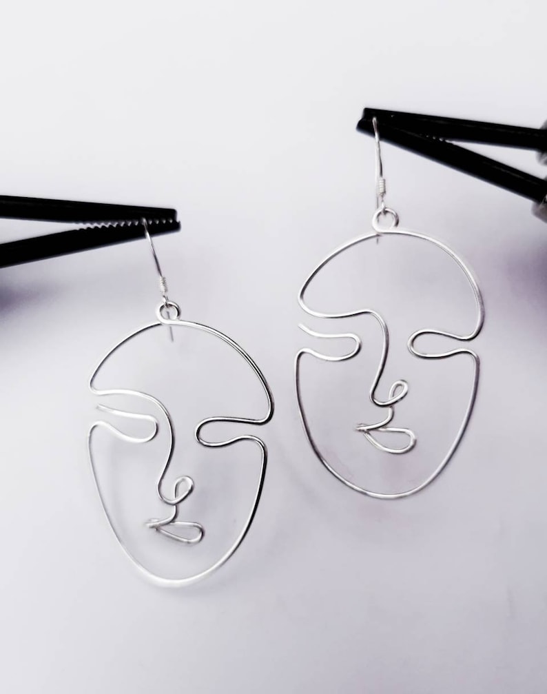 Boucles d’oreilles suspendues devant la tour Eiffel, capturant l’inspiration artistique et la finesse du travail artisanal.