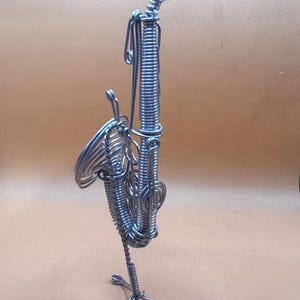 Vue verticale d’une sculpture de saxophone en métal torsadé, posée sur un fond beige.