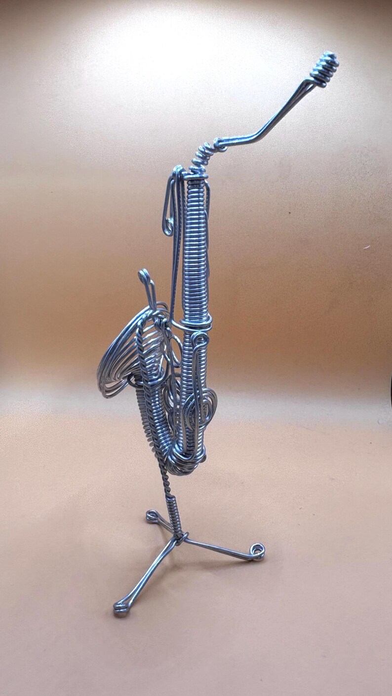 Vue verticale d’une sculpture de saxophone en métal torsadé, posée sur un fond beige.