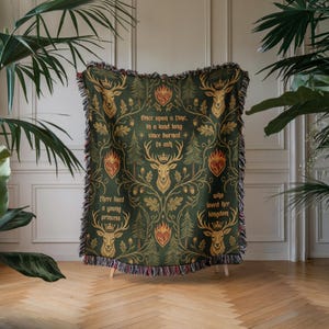 May include: A dark green throw blanket with a repeating pattern of deer, hearts, and foliage. The blanket has a decorative fringe and text that reads "Once upon a time..." and "There lived a young princess..."
