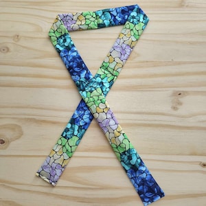 May include: A blue, green, yellow, and purple fabric ribbon with a stained glass pattern. The ribbon is tied in a knot.