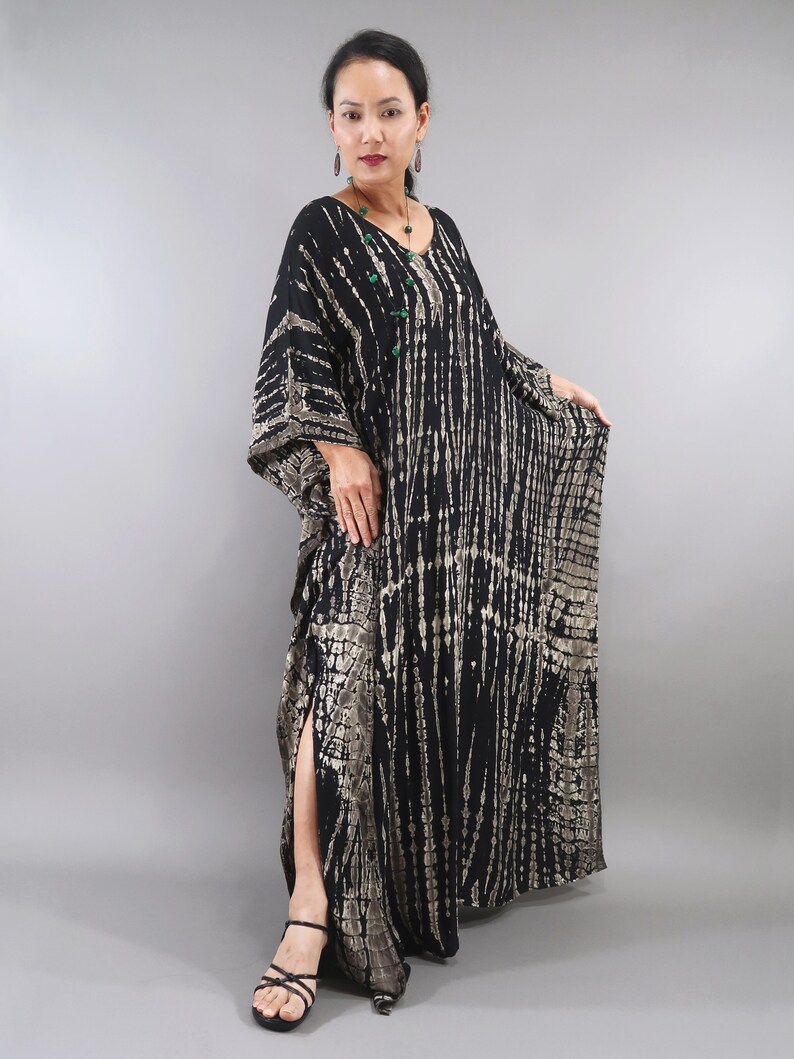 May include: A long black and silver tie-dye maxi dress with a V-neck and long sleeves. The dress has a side slit and is made of a soft, flowing fabric.
