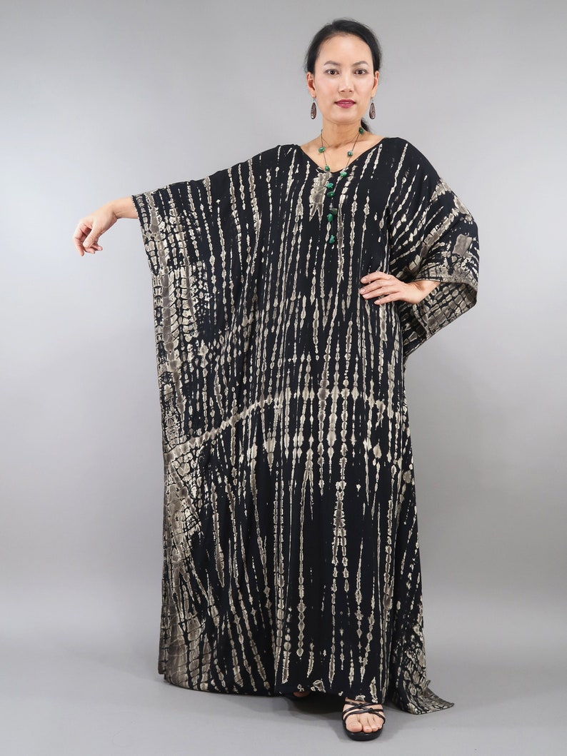 May include: A black and gold tie-dye kaftan with a V-neckline and long sleeves. The kaftan is made of a soft, flowing fabric and has a relaxed fit.