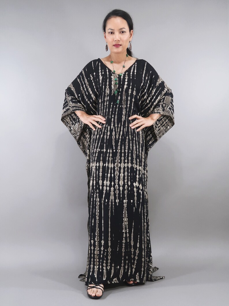 May include: A black and white tie-dye kaftan with a long, flowing silhouette. The kaftan features a V-neckline and a loose, comfortable fit. The model is wearing a green gemstone necklace and earrings.