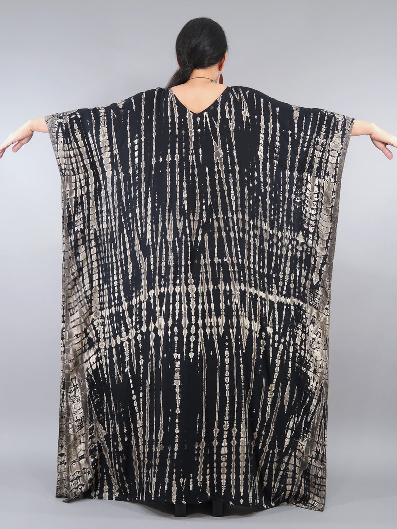 May include: Black and gold tie-dye kaftan with a V-neckline. The kaftan has a flowing, loose fit and is made of a soft, comfortable fabric.