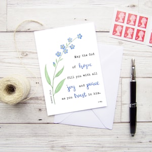 May include: A white card with a blue forget-me-not flower illustration and a quote from Romans 15:13. The quote reads: "May the God of hope fill you with all joy and peace as you trust in him."