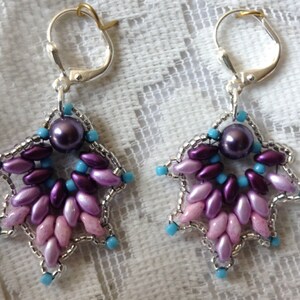 May include: A pair of silver earrings with a star-shaped design. The stars are made of purple, pink, and blue beads. Each star has a single pearl in the center.