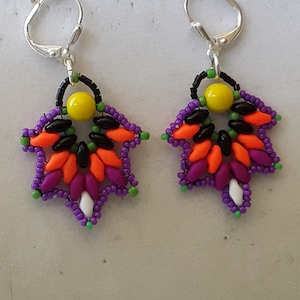 May include: A pair of beaded earrings with a starburst design. The earrings are made with purple, orange, green, black, white, and yellow beads. The earrings have silver hooks.