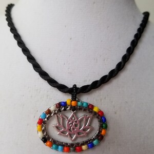 May include: A black cord necklace with a silver lotus flower pendant. The pendant is surrounded by a circle of colorful beads.