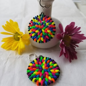 May include: A pair of colorful beaded earrings with a circular design. The earrings are made with small, bright beads in a variety of colors, including red, orange, yellow, green, blue, purple, and pink. The beads are arranged in a circular pattern, creating a vibrant and eye-catching design.