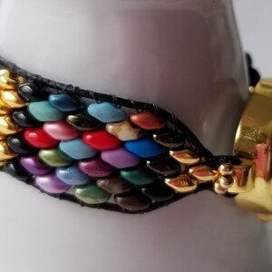 May include: A colorful beaded watch strap with a gold-tone watch face. The strap is made of small, colorful beads that are arranged in a chevron pattern. The watch face is round and has a gold-tone bezel.