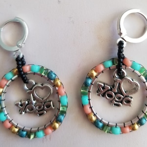 May include: A pair of silver hoop earrings with a beaded border in shades of turquoise, coral, and gold. The earrings feature a silver charm with the words "I love yoga" and a heart.