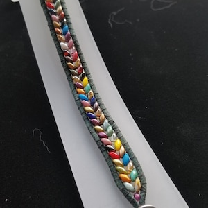 May include: A green leather bracelet with a colorful beaded design and an Om symbol charm.