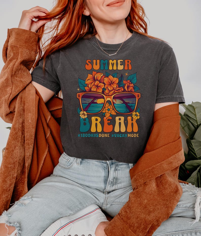 May include: A dark grey t-shirt with a retro-style graphic of sunglasses with a beach scene inside, flowers, and the text "Summer Break #180daysdone #vacaymode".