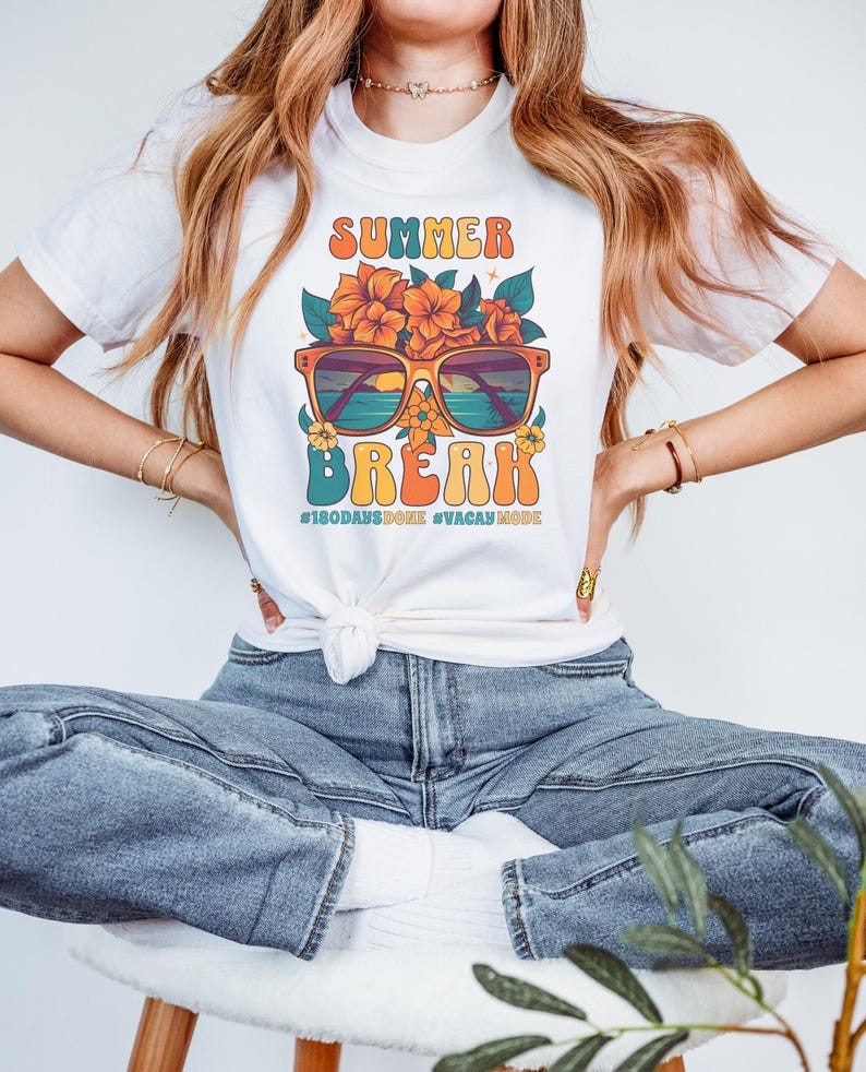 May include: White t-shirt with a retro graphic design featuring sunglasses with a beach scene inside, flowers, and the text "Summer Break #180daysdone #vacaymode".