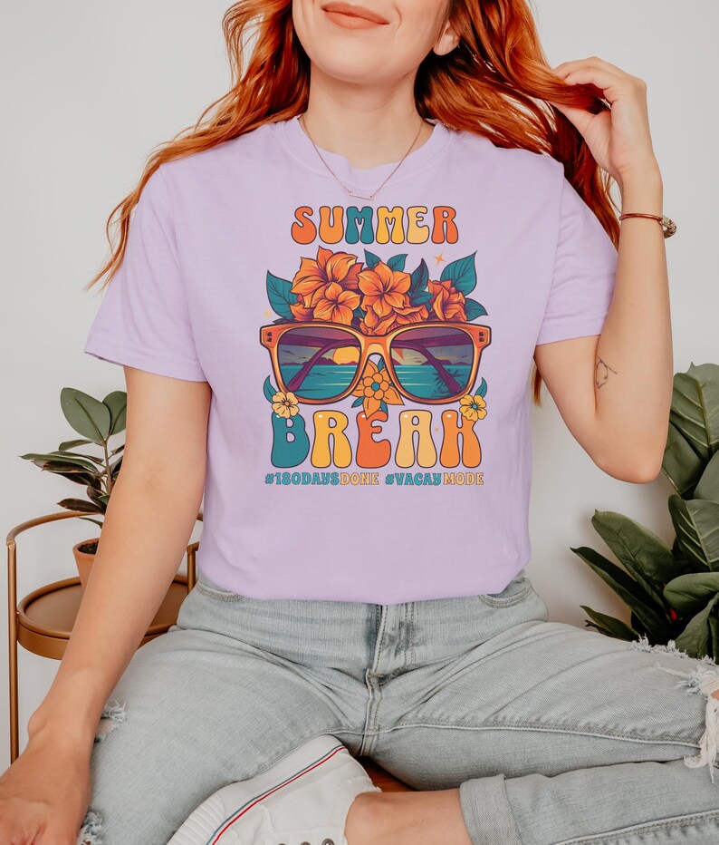 May include: A lavender t-shirt with a graphic design of sunglasses with a sunset and ocean scene, flowers, and the text "Summer Break #180DaysDone #VacayMode".
