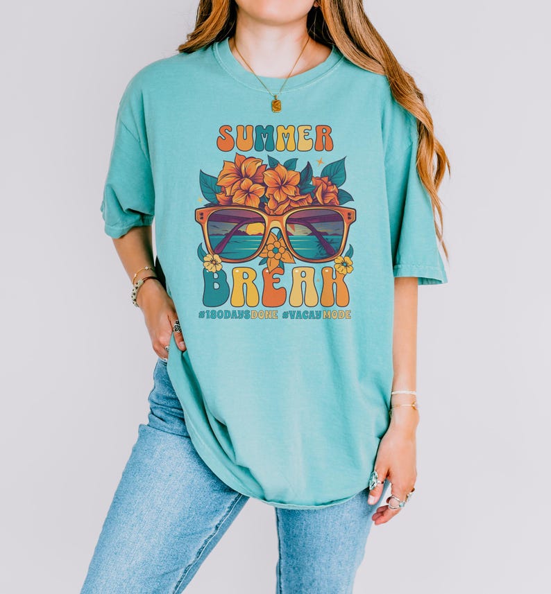 May include: A turquoise blue t-shirt with a retro graphic design featuring sunglasses with a sunset scene, flowers, and the text "Summer Break #180daysdone #vacaymode".
