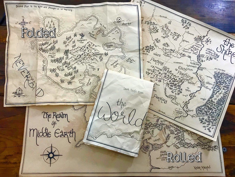 A photo of four maps that show how they look when they have been folded. They are sitting on a brown wooden surface. The two maps on the bottom are laying flat. The map in the top left of the photo is flat but crinkled. The map on top is folded.