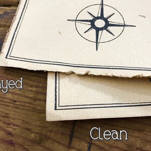 A close up of two maps resting on top of each other to show the corners and the edges. The map on top has frayed edges, while the map below has clean edges. Both are resting on a brown wooden surface.