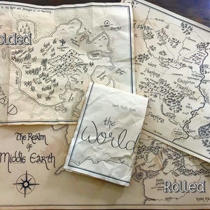 A photo of four maps that show how they look when they have been folded. They are sitting on a brown wooden surface. The two maps on the bottom are laying flat. The map in the top left of the photo is flat but crinkled. The map on top is folded.
