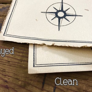 A close up of two maps resting on top of each other to show the corners and the edges. The map on top has frayed edges, while the map below has clean edges. Both are resting on a brown wooden surface.