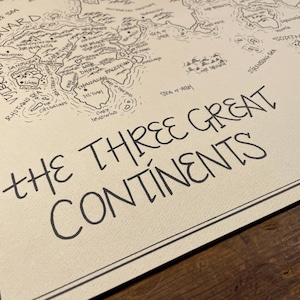 May include: A detailed black and white map titled "THE THREE GREAT CONTINENTS." The map features intricate illustrations of landmasses, seas, and islands, with handwritten place names. The map is on a cream-colored paper.