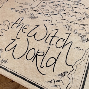 May include: A detailed map of "The Witch World" in black ink on aged paper. The map features stylized illustrations of landmasses, mountains, and other geographical features. The title is written in a whimsical font.