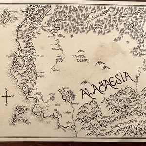 An overall picture of the map of Alagaesia, showing the hand-drawn details and writing. The paper is stained brown and the writing is black. The map is resting on a dark brown wooden surface.