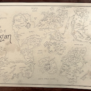 An overall picture of the map of Malazan, showing the hand-drawn details and writing. The paper is stained brown and the writing is black. The map is resting on a dark brown wooden surface.