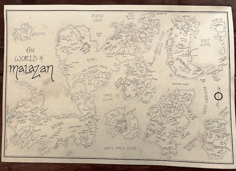 An overall picture of the map of Malazan, showing the hand-drawn details and writing. The paper is stained brown and the writing is black. The map is resting on a dark brown wooden surface.