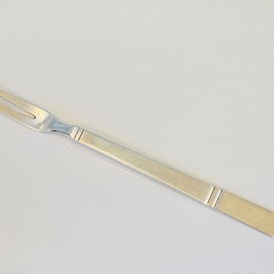 May include: A silver serving fork with two prongs and a long, slender handle. The handle has a subtle, textured design.