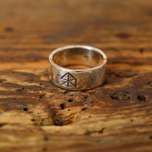 Könnte beinhalten: Ein silberner Ring mit gehämmerter Oberfläche und einem geometrischen Design. Der Ring liegt auf einer Holzoberfläche.