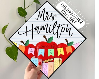 May include: A diamond-shaped graduation cap topper featuring a white lined paper background with the text Mrs. Hamilton in black script. Below, a red apple graphic displays a colorful banner with the text Class of 2027 and stacked books.