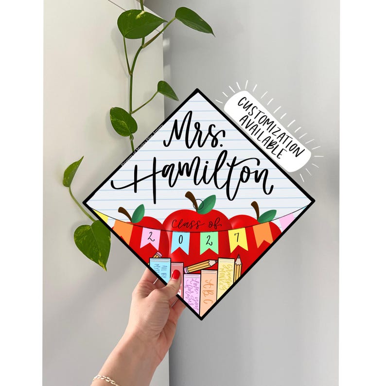 May include: A diamond-shaped graduation cap topper featuring a white lined paper background with the text Mrs. Hamilton in black script. Below, a red apple graphic displays a colorful banner with the text Class of 2027 and stacked books.