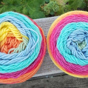 May include: Two skeins of rainbow colored yarn with a sparkly finish. The yarn is wound into a ball shape and is ready to be used for knitting or crocheting.