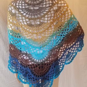 May include: A crocheted shawl with a colorful ombre design. The shawl is made with a variety of shades of blue, green, brown, and yellow yarn. The shawl is crocheted in a circular pattern with a scalloped edge.