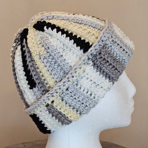 May include: A crocheted hat with a striped pattern in black, white, gray, and cream. The hat is folded over at the top and has a slouchy fit.