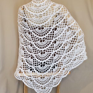 Puede incluir: Chale de ganchillo blanco con un diseño festoneado. El chal está hecho de un patrón delicado y calado y tiene una forma triangular.