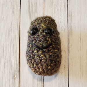 May include: A crocheted green, brown, and purple plush toy with black button eyes and a stitched-on smile.