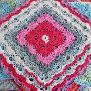 May include: A multi-colored crocheted blanket with a large, intricate, circular design in the center. The blanket is made up of several layers of different colors, including pink, red, white, gray, blue, and green.