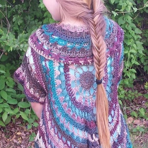 May include: A young person wearing a multi-colored crochet top with a braided hairstyle. The top is made with a variety of shades of brown, teal, and pink yarn. The top has a scalloped hem and a round neckline. The person is standing in front of a green leafy background. The text "Kriss Kcrochet" is visible in the upper right corner of the image.