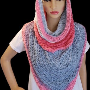 May include: A hooded crochet cowl scarf featuring a triangular drape design. The accessory is crafted with alternating bands of light gray and vibrant pink yarn, showcasing a textured stitch pattern with subtle openwork details along the edges.