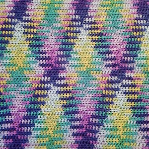 Puede incluir: Primer plano de una manta de ganchillo con un patrón geométrico en tonos de morado, rosa, verde, amarillo y blanco.