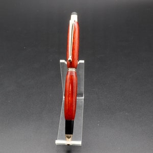 Front view of Bloodwood stylus pen with gold hardware on clear pen stand over black background