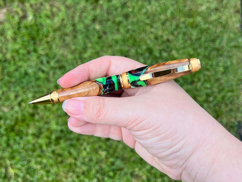 Holding olive wood and resin twist pen with satin gold hardware - in natural light