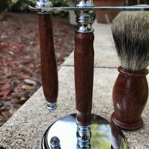 Eucalyptus shaving set with brush, stand, and razor handle sitting outside on a paver stone with grass in the background