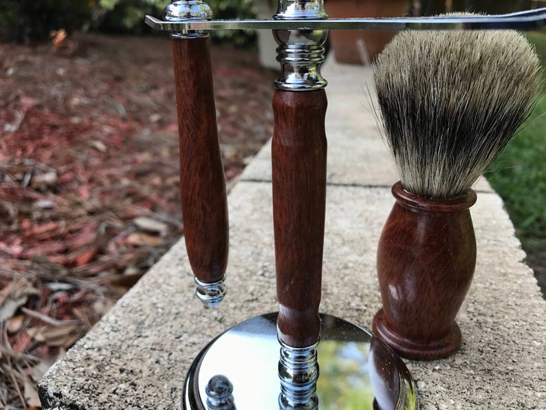 Eucalyptus shaving set with brush, stand, and razor handle sitting outside on a paver stone with grass in the background